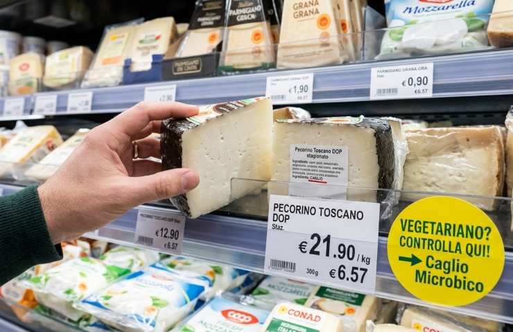 Mano sceglie Pecorino in supermercato, evidenziando etichetta con 'CAGLIO' e bollino giallo 'Vegetariano? Caglio Microbico'.