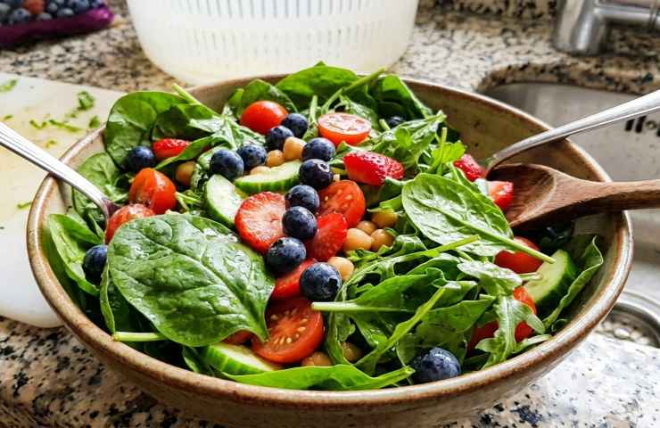 nsalata vegetariana fresca e colorata in ciotola rustica su bancone cucina. Primo piano realistico di rucola, spinaci, mirtilli e fragole.