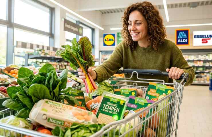 Donna felice fa la spesa vegetariana da Lidl, Aldi ed Esselunga con carrello pieno di prodotti Vemondo, tempeh e verdure fresche.