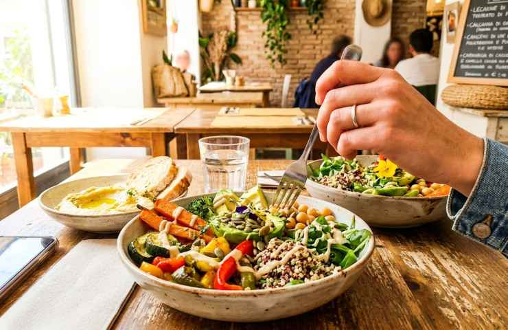 Primo piano luminoso e ravvicinato di una ricca e colorata bowl vegetariana con verdure arrosto, ceci e quinoa, servita in un locale rustico e accogliente pieno di luce naturale, perfetta per scoprire opzioni vegetariane vicino a me.