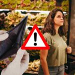 Donna al supermercato davanti al banco verdura con portafoglio vuoto e segnale di pericolo: analisi del risparmio sui piatti vegetariani a marzo 2026.